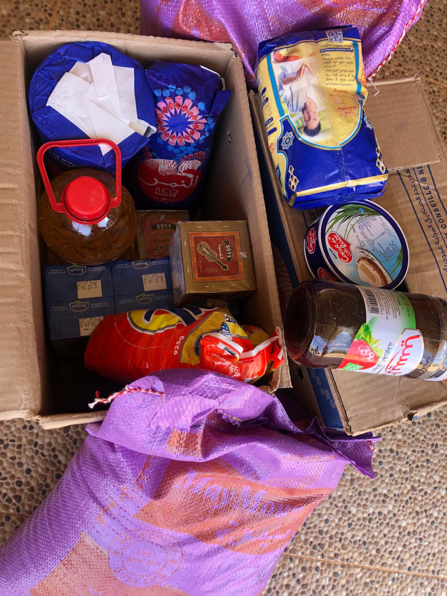 Panier contenant des produits alimentaires essentiels tels que farine, huile, sucre, et thé, préparé pour une distribution solidaire au Domaine Berraha, Sefrou, Maroc.