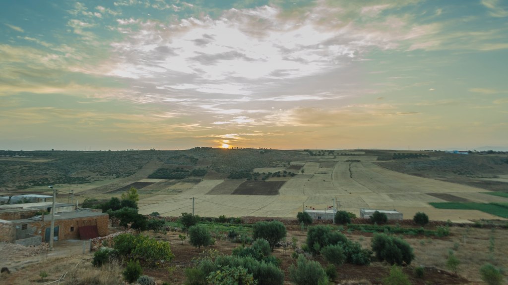 Lever de soleil sur le Domaine Agricole Berraha, offrant une vue panoramique sur les champs cultivés et les collines environnantes à Sefrou, Maroc.